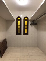 Un baño limpio con baldosas, dos ventanas de arco y un toallero para la ducha colgado.
