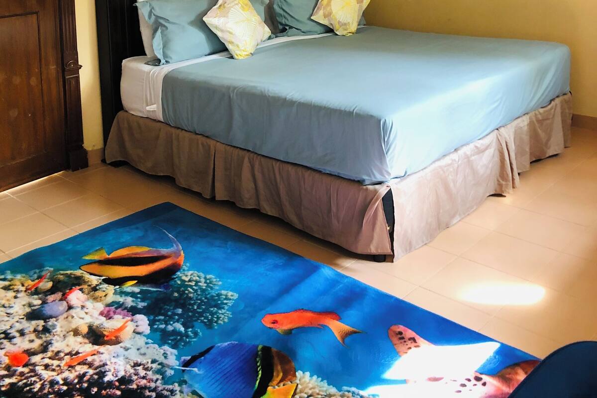 A bedroom with a bed, a ceiling fan, a painting of a sunset, and a seahorse painting.