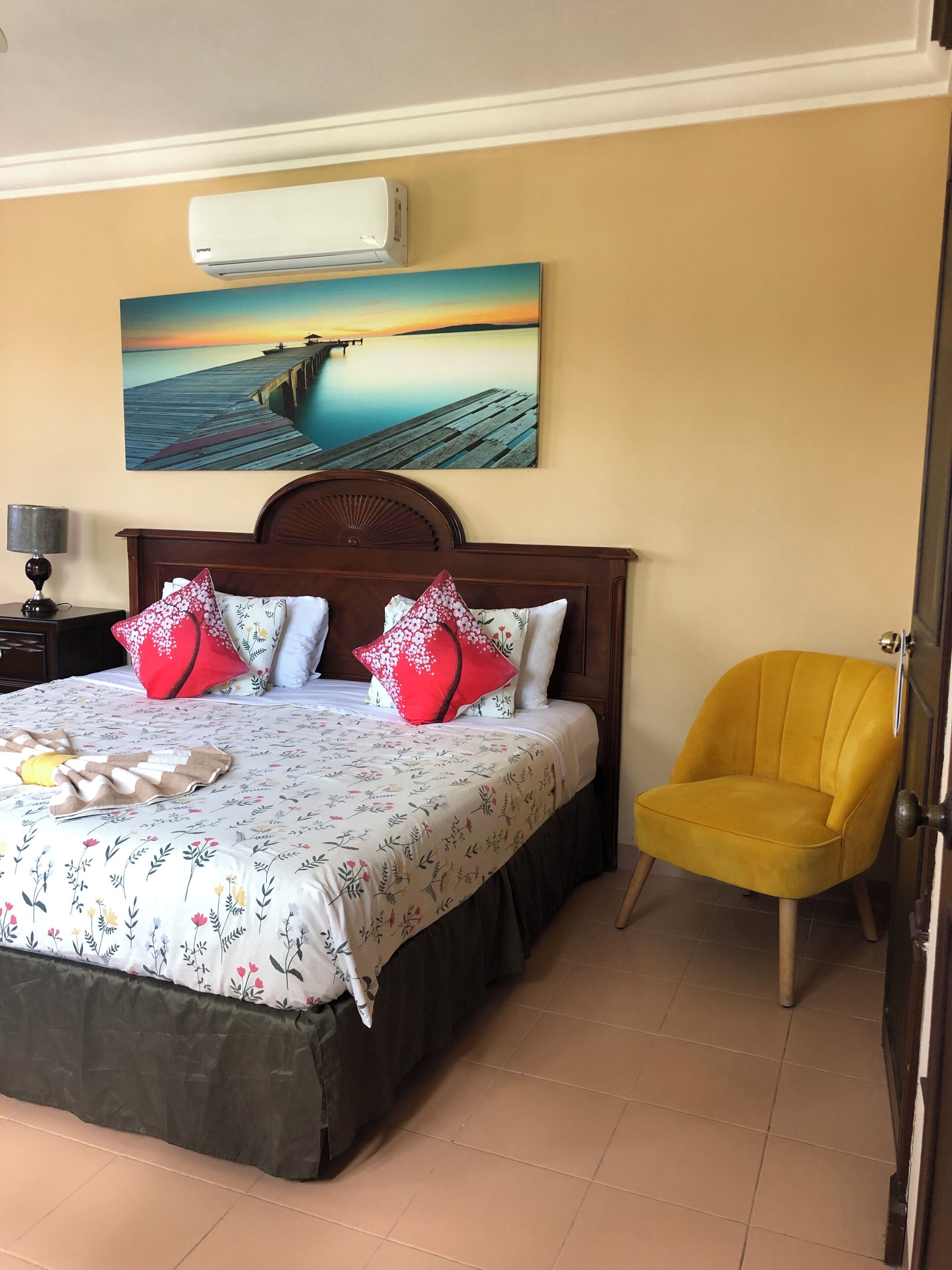 A neatly made bed with floral bedding, a wooden headboard, and a painting of a pier over water.