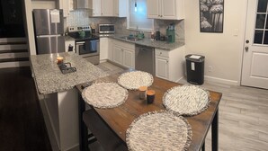 A modern kitchen with white cabinets, granite countertops, stainless steel appliances, and a dining area with a wooden table and woven placemats. - Family-Friendly Home with Downstairs Suite (Decatur)