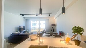 Eine moderne Küche mit einer zentralen Kochinsel, einem Essbereich mit einer Couch und Stühlen, einem Fernseher und Blick ins Freie.