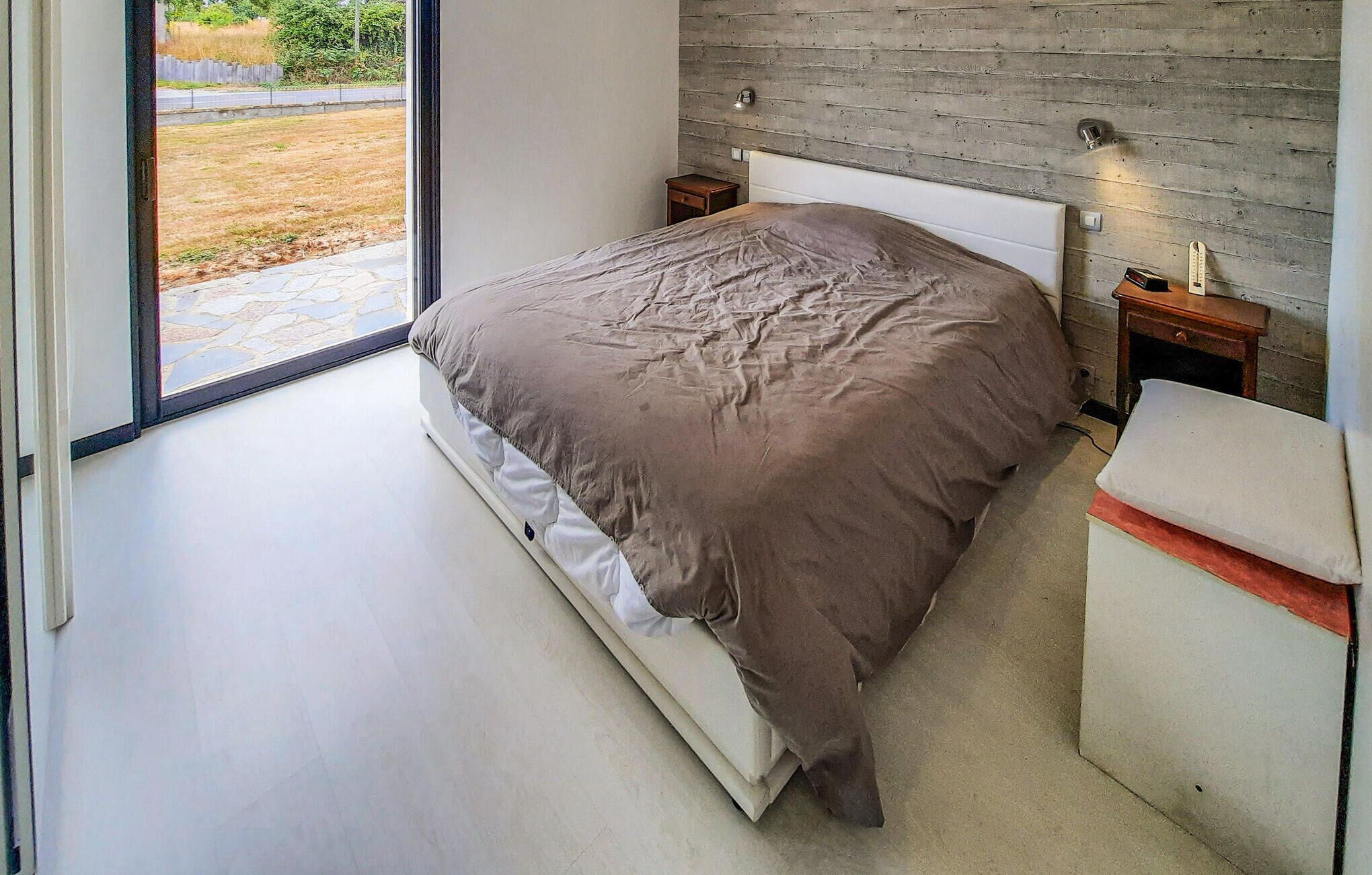 Een moderne slaapkamer met een groot bed, een houten hoofdbord, een nachtkastje en een bankje.