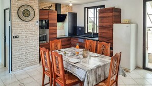 A dining area with a marble table, wooden chairs, a clock on the wall, and a kitchen in the background. - 2 bedroom stunning home in Bacilly (Bacilly)
