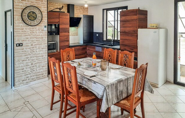 A dining area with a marble table, wooden chairs, a clock on the wall, and a kitchen in the background. - 2 bedroom stunning home in Bacilly (Bacilly)