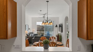 Uma cozinha moderna com armários de madeira, uma área de jantar com mesa branca e um ventilador de teto.