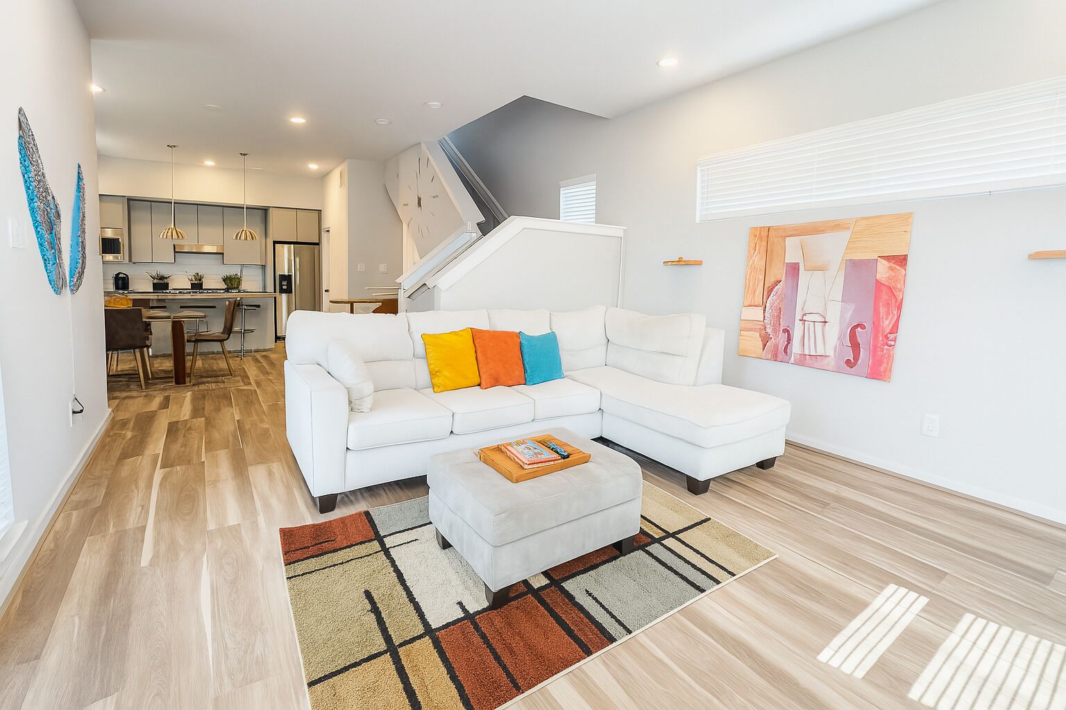 A modern living room with a white sectional sofa, a coffee table, and a staircase leading to an upper level.