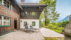Ett traditionellt trähus med en uteplats, utomhusmöbler och utsikt över bergen.
