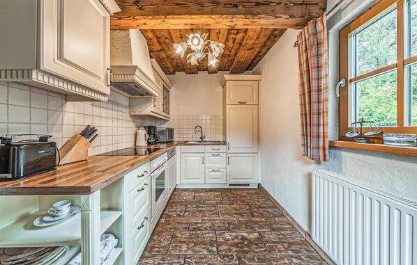 A compact kitchen with white cabinetry, a wooden countertop, and a window with plaid curtains.