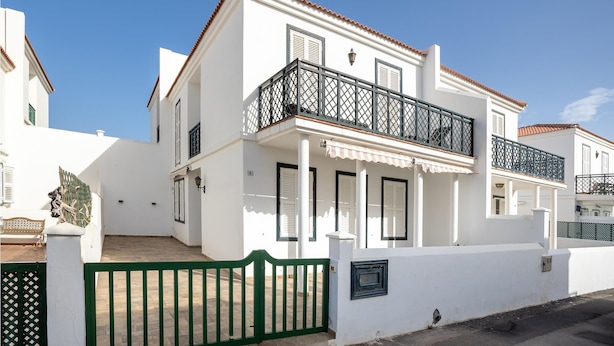 Un bâtiment blanc à deux étages, doté d’un balcon, d’un portail vert et d’un toit recouvert de tuiles.
