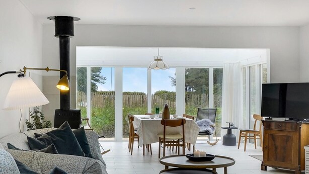 Una sala moderna con un sofá, una mesa de comedor con sillas, un televisor y un amplio ventanal con vistas al exterior.