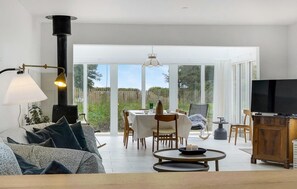 Una sala moderna con un sofá, una mesa de comedor con sillas, un televisor y un amplio ventanal con vistas al exterior.