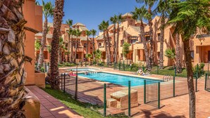 Area piscina con vasca rettangolare, circondata da palme e da una recinzione.