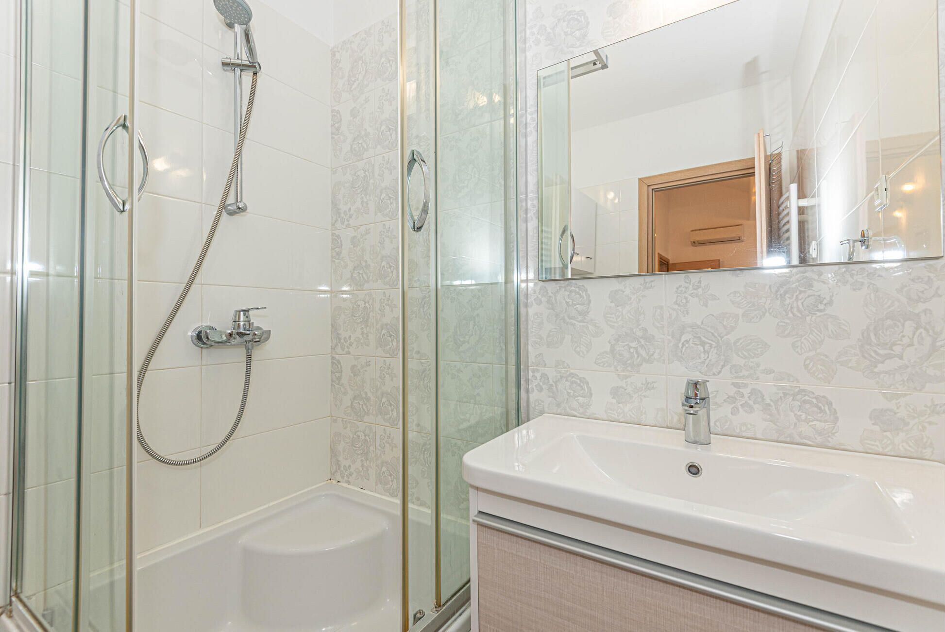 Une salle de bain moderne avec une douche à l’italienne en verre, un lavabo blanc et un miroir qui reflète un meuble en bois.
