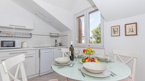Une cuisine moderne avec des meubles blancs, un four à micro-ondes et un lave-vaisselle. On y trouve une table à manger avec des assiettes, des verres et un panier de fruits.