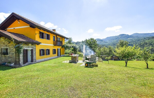 Un edificio amarillo de paredes de piedra, una chimenea de piedra y un pequeño jardín con una parrilla y un paraguas blanco.