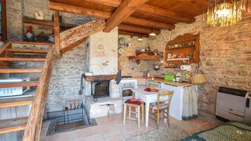Una cucina rustica con parete in pietra, travi in legno, camino e una scala in legno.