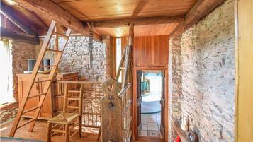 Interno accogliente di una baita in legno, con parete in pietra, una scala in legno e vista sul bagno.