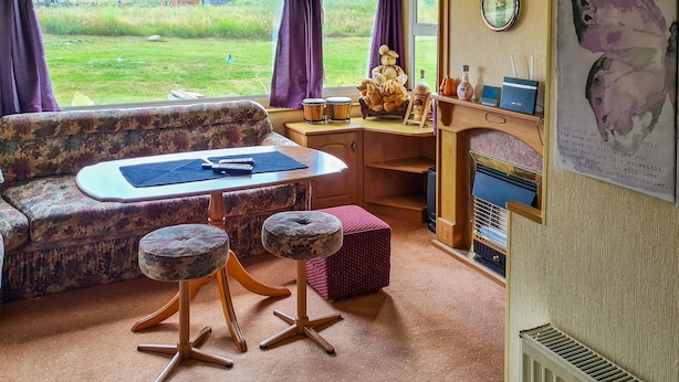 Un intérieur chaleureux avec un canapé, une petite table, deux poufs, une horloge et une cheminée.
