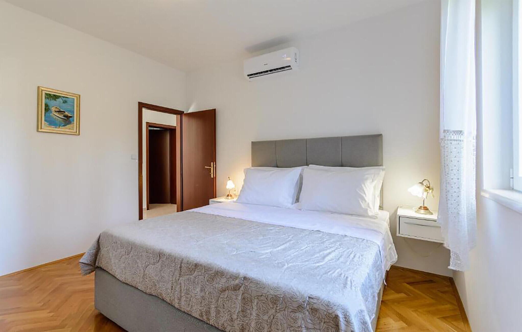 Une chambre d’hôtel comprenant un lit, des tables de chevet, un appareil de climatisation, une porte et une fenêtre avec des rideaux.