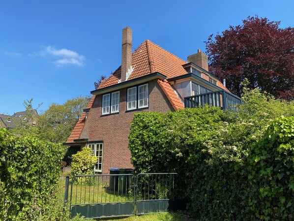 A two-story house with a brick facade, a red-tiled roof, and a visible chimney.