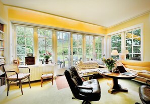 A bright room with large windows, a sofa, a chair, a table, and a bookshelf.