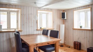 Een kamer met houten lambrisering, een eettafel met stoelen, een staande lamp, een aan de muur bevestigde televisie en een koffer op de vloer.