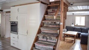Een trap met een uniek geweven ontwerp, een keukenhoek met een inbouwoven, en een woonruimte met een bank en een tafel.
