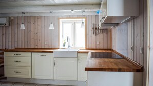 Een keuken met houten kastjes, een houten aanrecht, een spoelbak en hangende lampen.