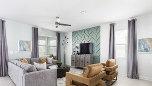Een moderne woonkamer met een grijze bank, een beige fauteuil, een salontafel en een tv op een kast.