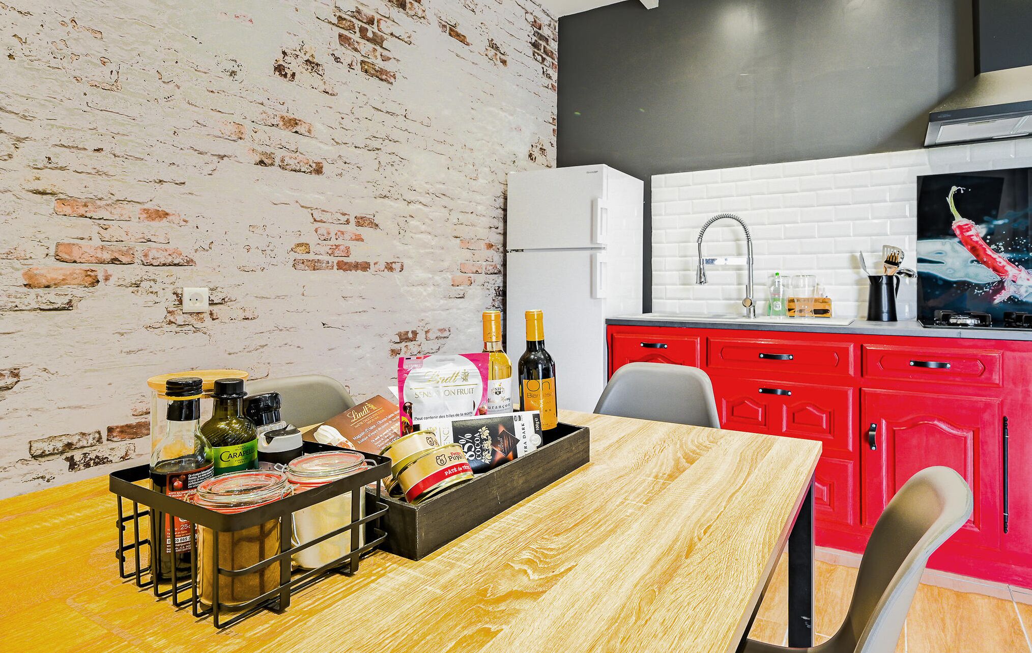 A kitchen with a brick wall, red cabinets, and a wooden dining table with condiments and bottles.
