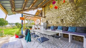A covered outdoor seating area with a stone wall, a tiled floor, and a table with chairs.