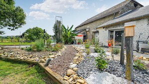 A rustic stone building with a garden in front, featuring a variety of plants and a small pond.