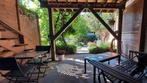 A covered patio with a table and chairs, a wooden pergola, and a view of a garden.