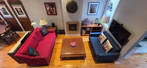 Een woonkamer met een rode bank, een blauwe bank, een houten salontafel, een open haard en een televisie.