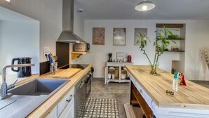 Une cuisine moderne dotée d’un évier en acier inoxydable, d’un four encastré, d’un four à micro-ondes et d’une machine à café. On y trouve un plan de travail en bois, un luminaire suspendu et une petite plante posée sur le plan de travail.