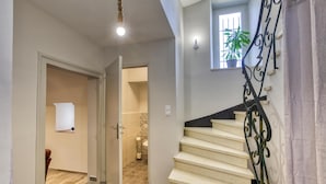 Un escalier avec une rampe en métal noir, une porte donnant sur une salle de bain et une petite fenêtre ornée d’une plante.