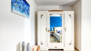 Une pièce avec une armoire blanche, un lit doté d’une tête de lit bleue et un tableau abstrait bleu accroché au mur.