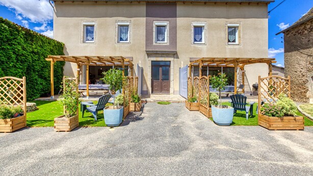 Un bâtiment à deux étages doté d’une entrée centrale, de deux espaces extérieurs abrités avec des pergolas en bois, et d’une allée gravillonnée.