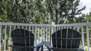 Um terraço com duas cadeiras Adirondack voltadas para uma floresta.