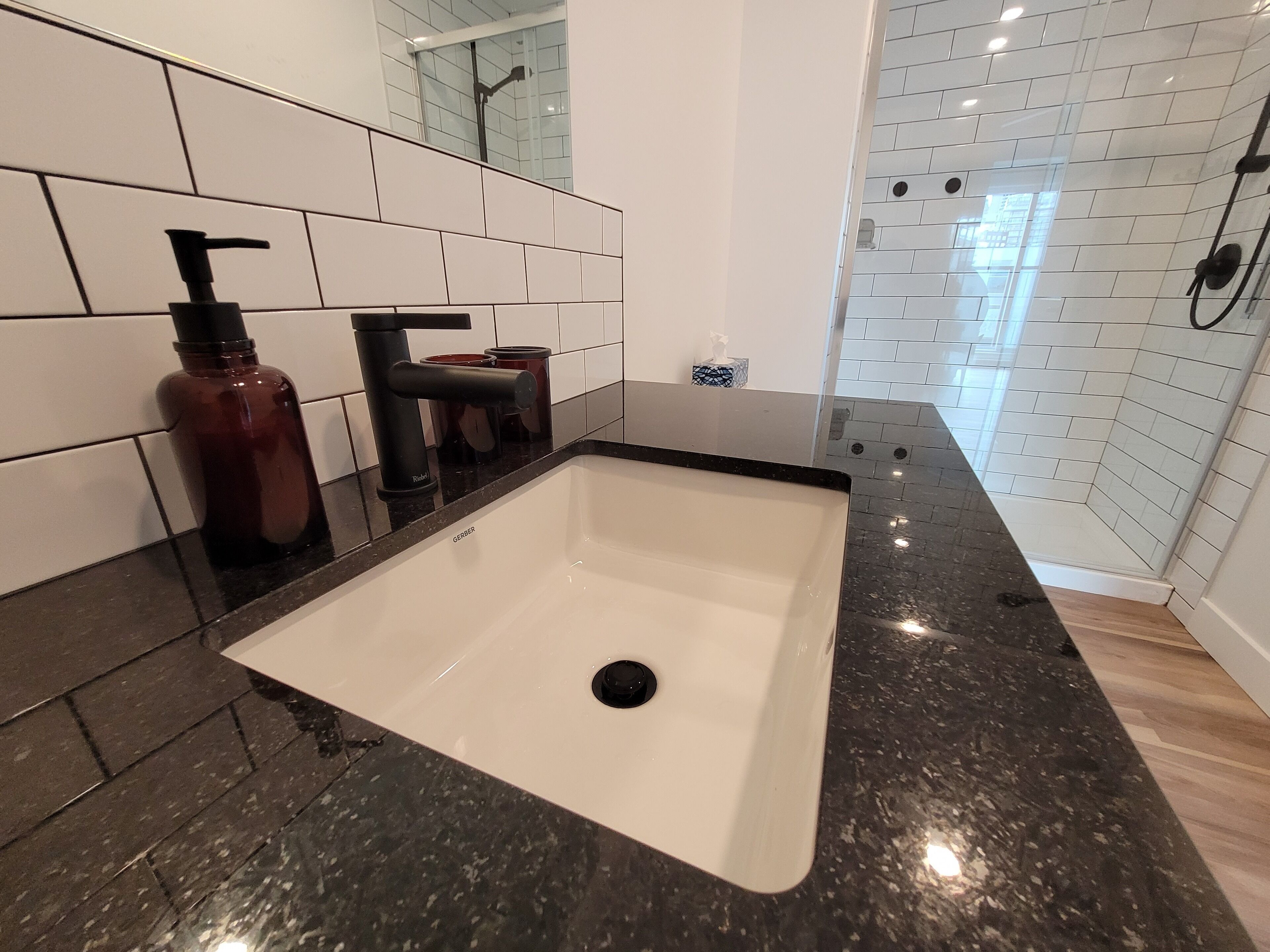 Une salle de bain avec un lavabo blanc, un robinet noir et un miroir au-dessus.