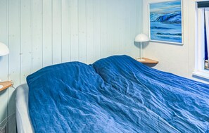 Een kamer met een bed belegd met een blauwe deken, een nachtkastje met een lamp en een schilderij aan de muur.