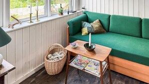 A cozy room with a green sofa, a small wooden table with magazines, a wicker basket, and a window with decorative items. - 2 bedroom nice home in Aabenraa (Aabenraa)
