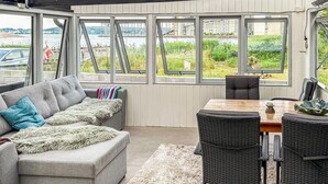 A cozy room with a grey sofa, a wooden table, and wicker chairs. Large windows offer a view of a body of water and greenery. - 2 bedroom nice home in Aabenraa (Aabenraa)