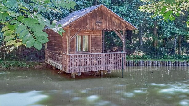 Una baita di legno con un balcone, immersa nell'acqua e nel verde.