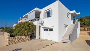Una casa moderna blanca de dos pisos con un muro de piedra, una antena parabólica y una escalera que conduce al piso superior.