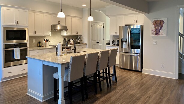 A modern kitchen with white cabinets, stainless steel appliances, a central island with bar stools, and pendant lighting. - Spacious New Home, Minutes to Augusta National! (North Augusta)