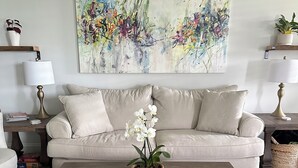 A living room with a beige sofa, a wooden coffee table, a potted orchid, and abstract art on the wall. - Spacious New Home, Minutes to Augusta National! (North Augusta)