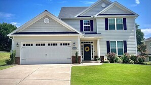 A two-story house with a white garage door, a front porch with a wreath, and a well-maintained lawn. - Spacious New Home, Minutes to Augusta National! (North Augusta)