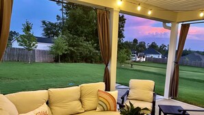 A covered patio area with a beige sofa, a small table, and a chair. - Spacious New Home, Minutes to Augusta National! (North Augusta)