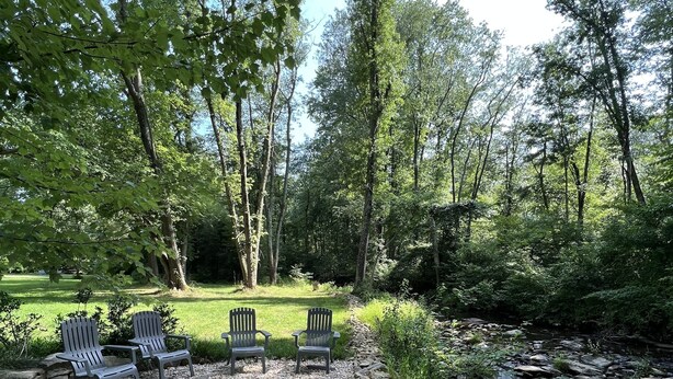 A serene outdoor seating area with chairs and a fire pit, surrounded by a stone wall and a small stream. - Historic Schoolhouse on Winery Row (Purcellville)